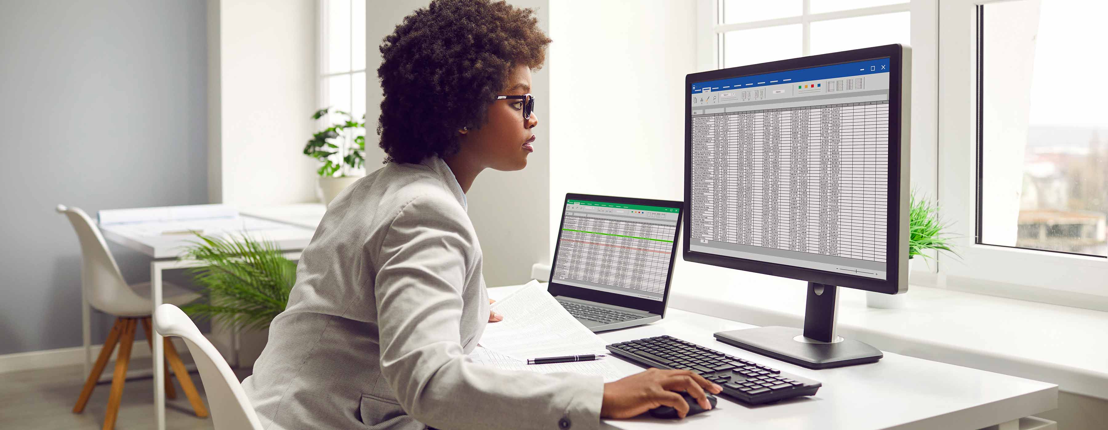 Formação em Excel do Básico ao Avançado - Foto de mulher usando óculos olha para tela de computador que exibe uma tabela Excel